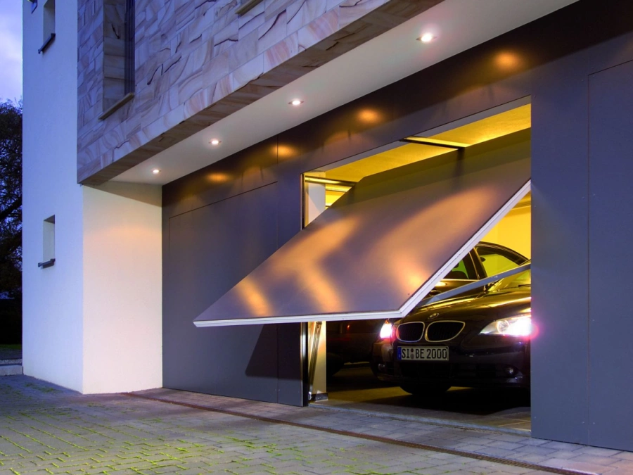 Porte de garage basculante anthracite AFC entrouverte de nuit, villa contemporaine à Caen.