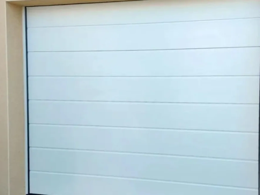 Porte de garage sectionnelle blanche Hormann motorisée sur façade crème, installation résidentielle AFC dans le Calvados.
