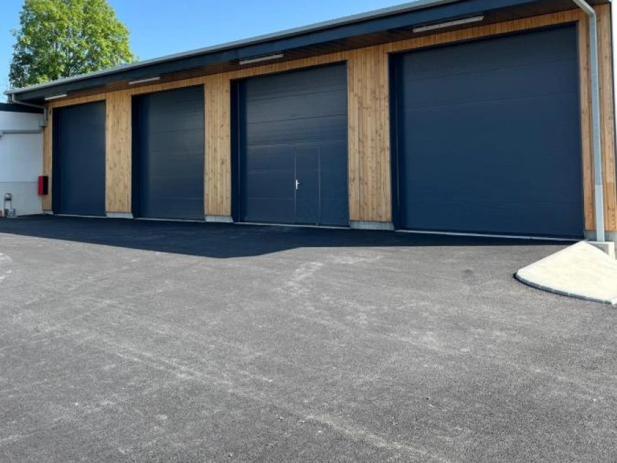 Quatre portes sectionnelles motorisées anthracite avec portillon intégré sur bardage bois, bâtiment professionnel AFC Caen.