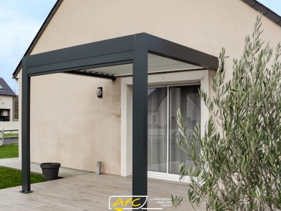 Pergola bioclimatique aluminium anthracite adossée à une maison, terrasse aspect bois et olivier, AFC Calvados.