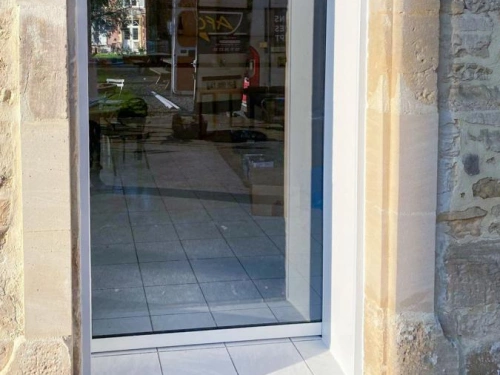 Baie vitrée aluminium claire dans mur pierre de Caen, reflet fourgon AFC, porte automatique