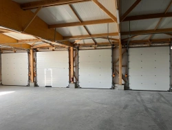 Intérieur d'un hall industriel avec portes sectionnelles blanches motorisées et portillon, charpente bois, AFC Calvados.