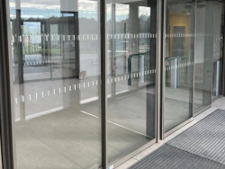 Portes automatiques coulissantes en verre vues depuis le hall, capteurs et tapis d'entrée, pose AFC Calvados.