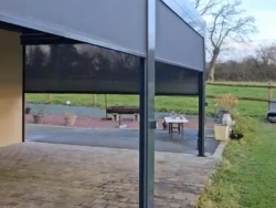 Stores zip motorisés partiellement baissés sur pergola bioclimatique anthracite, vue jardin Calvados, AFC.