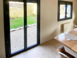 Porte-fenêtre et fenêtre anthracite vues de l'intérieur, jardin et mur en pierre normand, menuiseries AFC Caen.