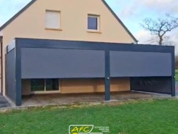 Pergola aluminium anthracite avec stores verticaux partiellement baissés sur terrasse, jardin résidentiel AFC près de Caen.