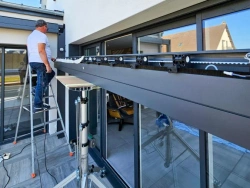 Pose du profilé aluminium d'une pergola Open'R sur baie vitrée, technicien AFC sur échelle