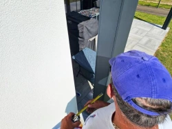 Technicien AFC mesurant un poteau de pergola anthracite sur terrasse carrelée, Calvados