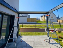 Structure de pergola Open'R anthracite en montage sur terrasse, maison moderne Normandie