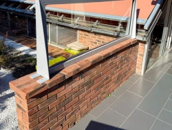 Paroi vitrée fixe aluminium sur muret brique, store banne orange en fond, terrasse Calvados