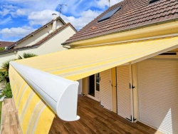 Store banne rayé jaune et blanc avec coffre blanc, ombre sur terrasse bois, pose AFC