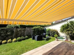 Vue sous store banne jaune orange et blanc protégeant terrasse et jardin, Calvados