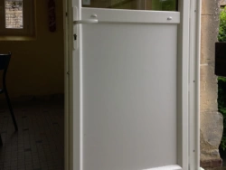 Porte de service PVC blanche semi-vitrée ouverte sur une cour en pierre, réalisation AFC Normandie