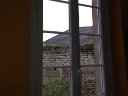 Fenêtre PVC blanche à petits bois vue de l'intérieur, jardin et mur en pierre en Normandie
