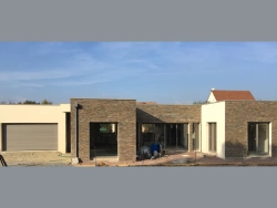 Façade contemporaine avec porte de garage grise et baies anthracite, chantier AFC dans le Calvados