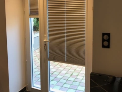 Porte-fenêtre blanche vue de l'intérieur avec stores plissés et panneau fixe, réalisation AFC Caen