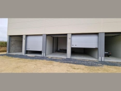 Portes industrielles sectionnelles grises mi-ouvertes sur box de stockage professionnels près de Caen