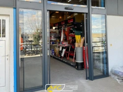 Porte automatique vitrée ouverte sur magasin de fournitures, menuiserie aluminium anthracite AFC
