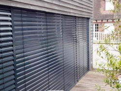 Brise-soleil orientable aluminium gris sur grande baie vitrée et terrasse bois, Normandie